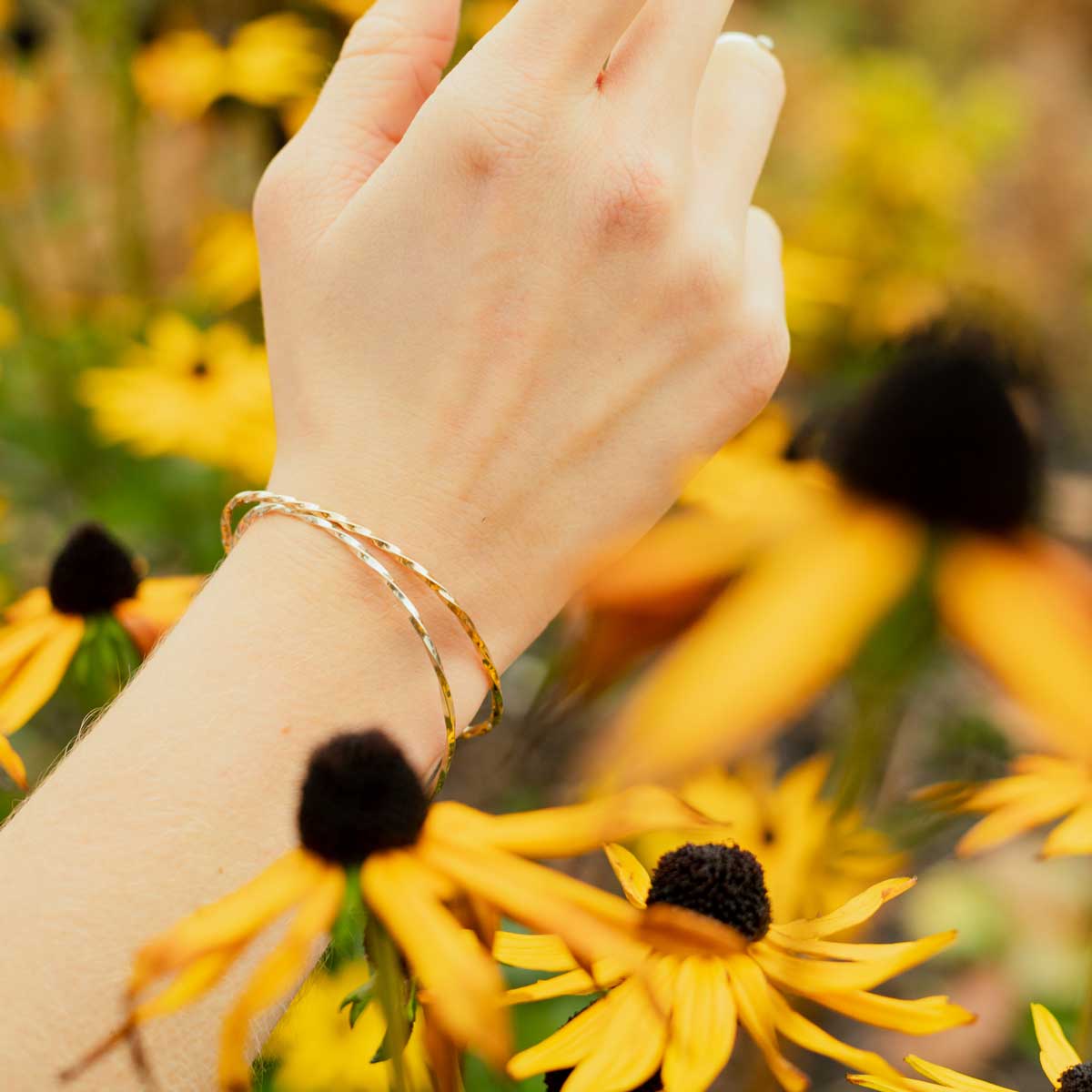 Gold and silver twisted torc bracelets being worn on a wrist in a field full of flowers