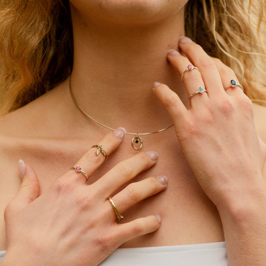 Close up of a 14k gold sapphire and diamond omega necklace being worn by a girl with gold and silver rings on her fingers.