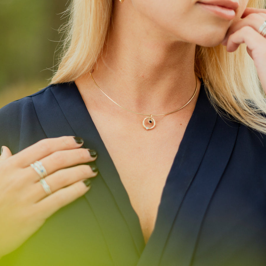 Blonde girl in a natural setting in a blue dress, wearing a gold necklace.