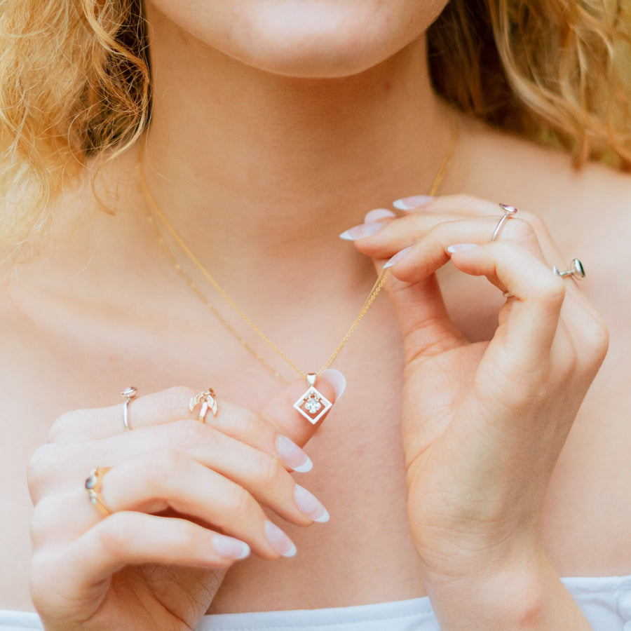 Model wearing a gold faileas necklace with white princess cut sapphire.