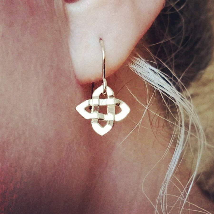 Side view of a gold celtic cross earring being worn.