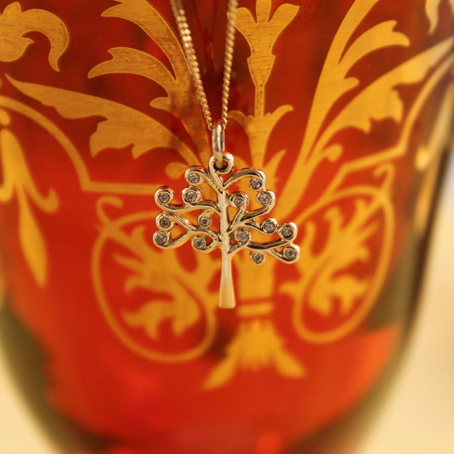 solid gold yggdrasil necklace hanging in front of a vase.