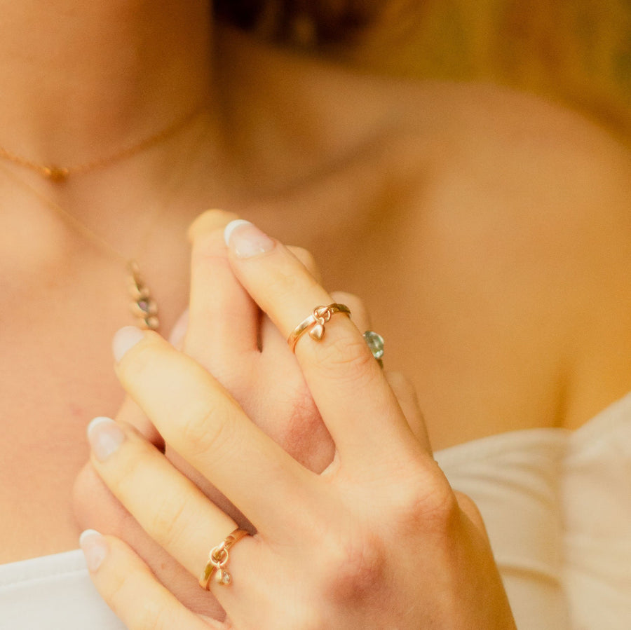 Model wearing a solid gold heart drop ring with charm