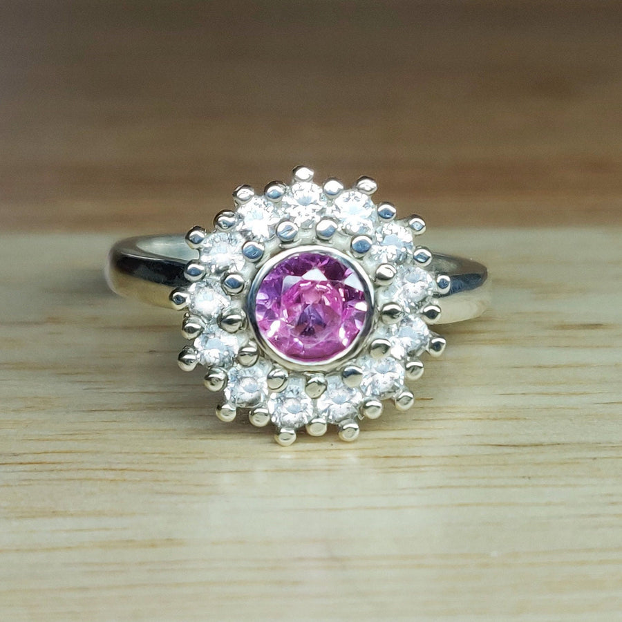 Front view of a pink and white sapphire pave cluster halo ring on a wooden surface.