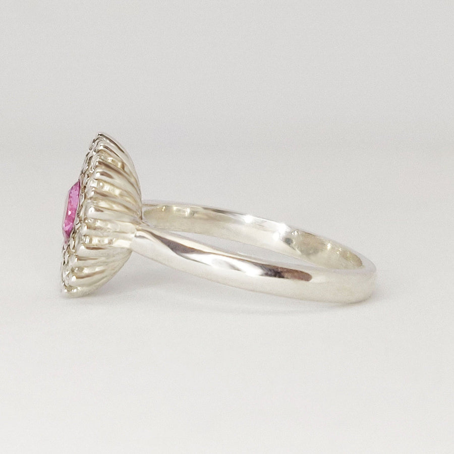 Side view of a pink and white sapphire pave cluster halo ring on a white background.