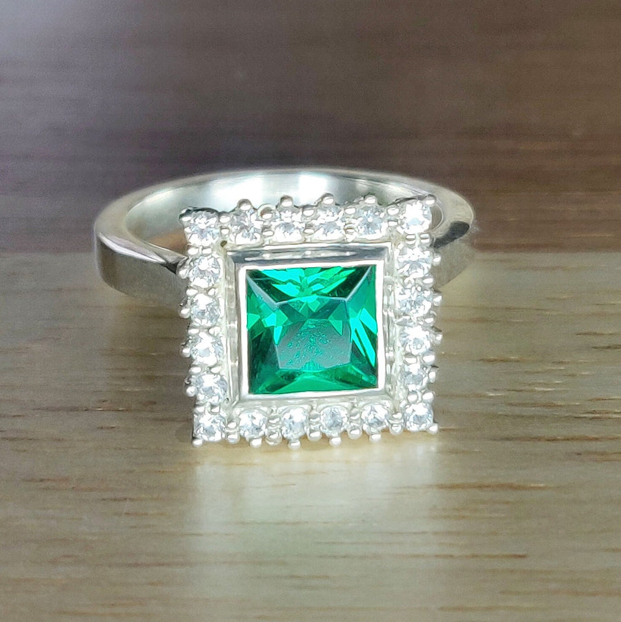 Front view of a princess cut emerald and diamond halo cluster ring on a wooden surface.