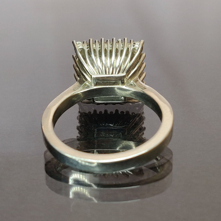 Rear view of a princess cut emerald and diamond halo cluster ring on a reflective surface.