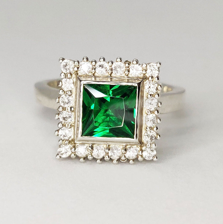 Front view of a princess cut emerald and white diamond halo cluster ring on a white background.