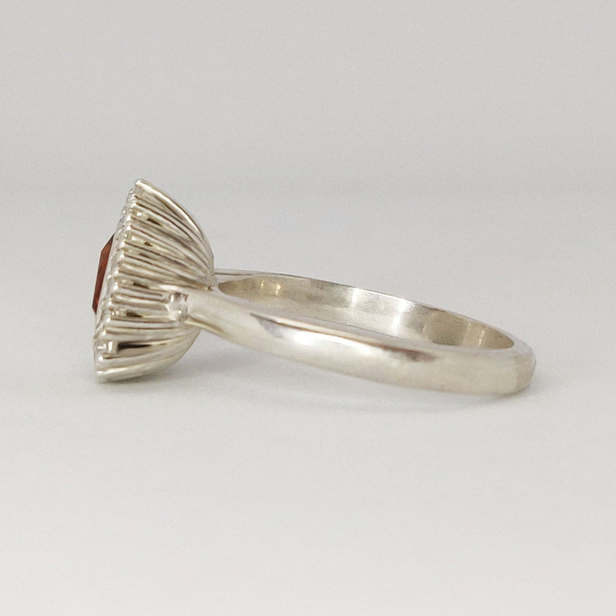 Side view of a trillion cut citrine and white sapphire halo cluster pave ring on a white surface.