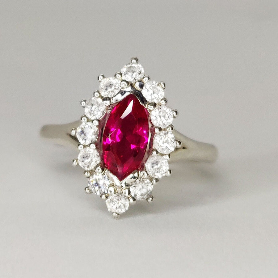Front view of a marquise ruby and white sapphire pave set cluster halo ring on a white background.