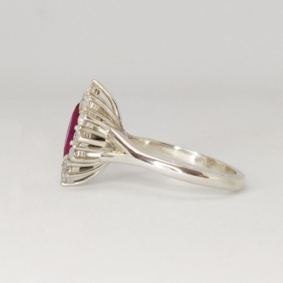 Side view of a marquise ruby and white sapphire pave set cluster halo ring on a white background.
