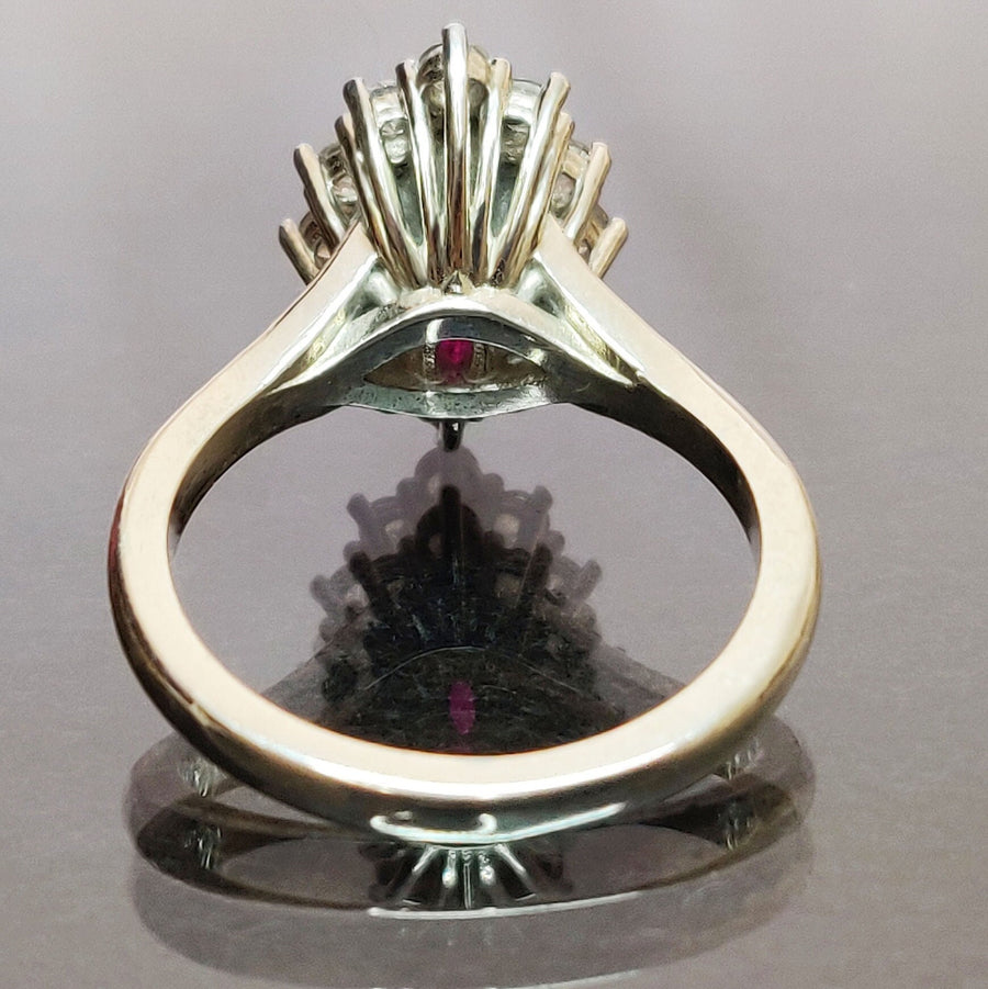 Rear view of a marquise ruby and white sapphire pave set cluster halo ring on a reflective surface.