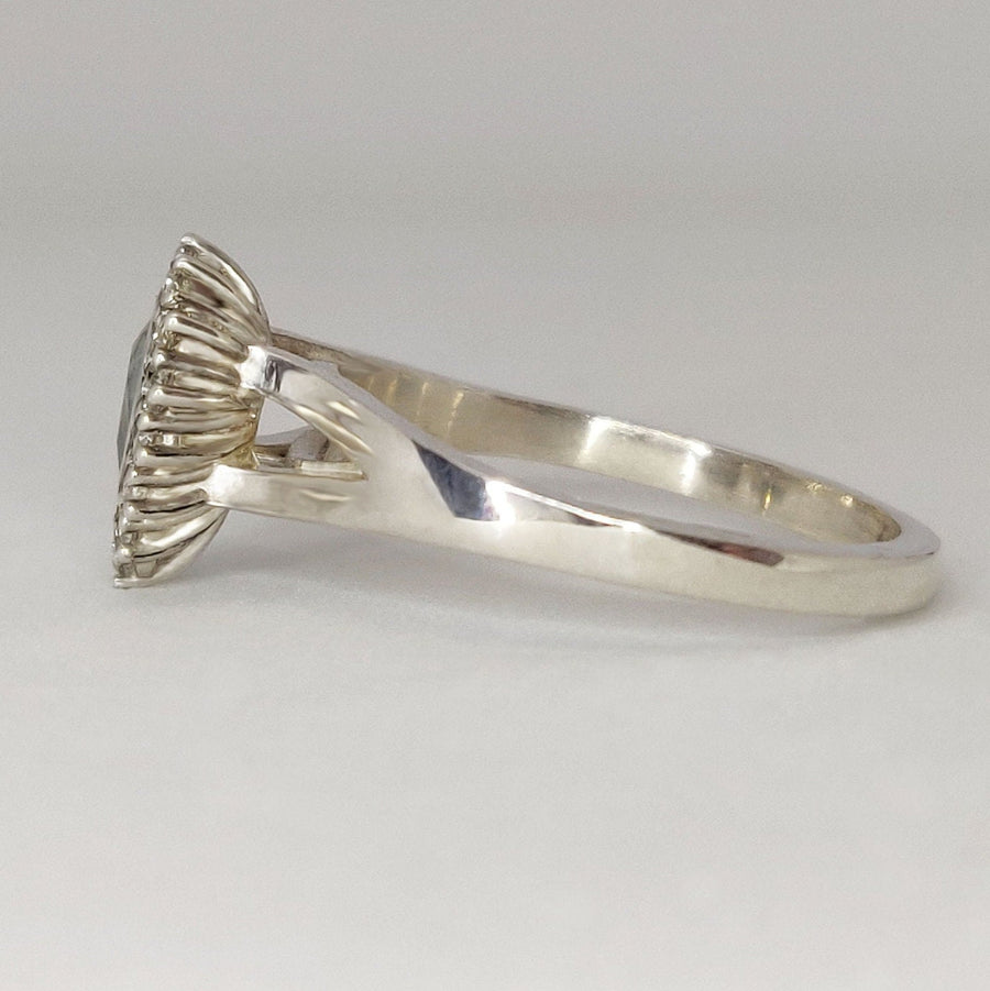 Side view of a pear cut aquamarine and white sapphire halo cluster ring on a white surface.