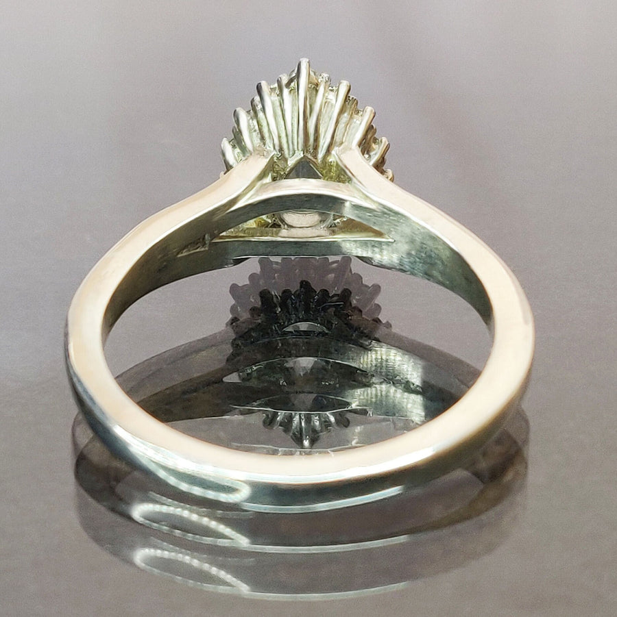 Rear view of a pear cut aquamarine and white sapphire halo cluster ring on a reflective surface.