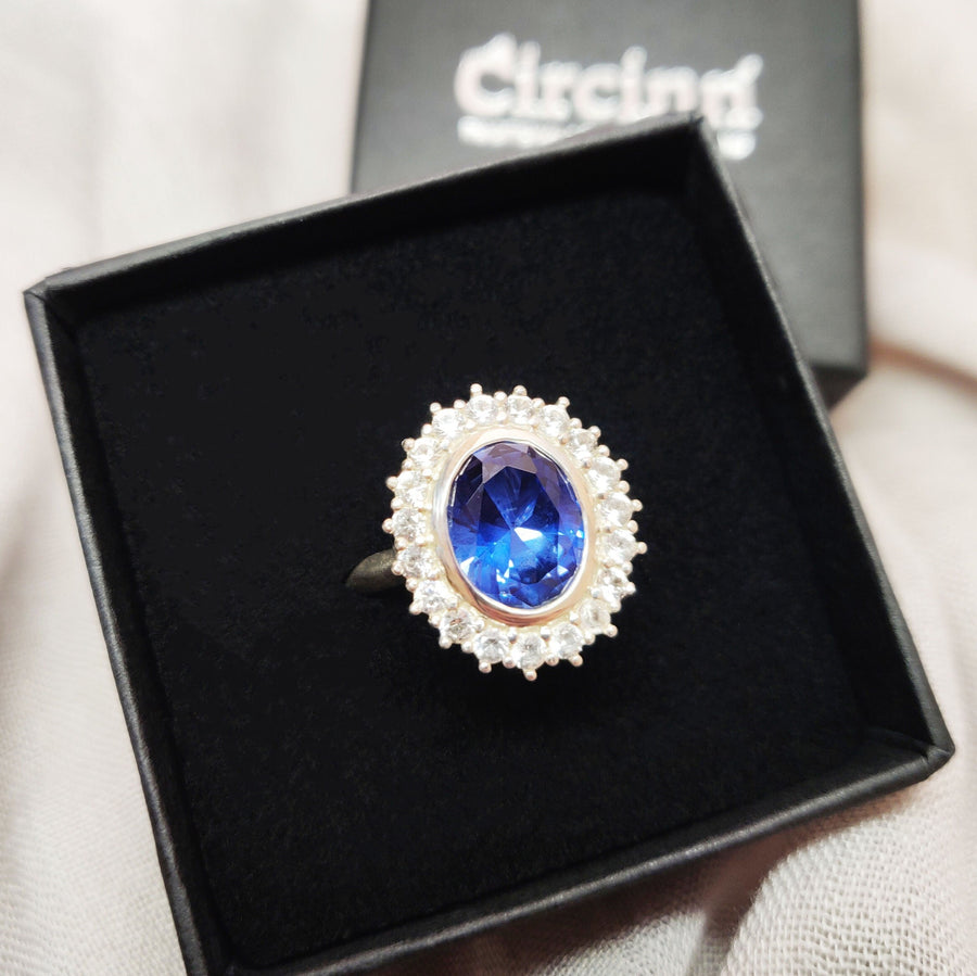 Bezel set blue and white sapphire halo cluster ring in a branded Circinn Ring box.