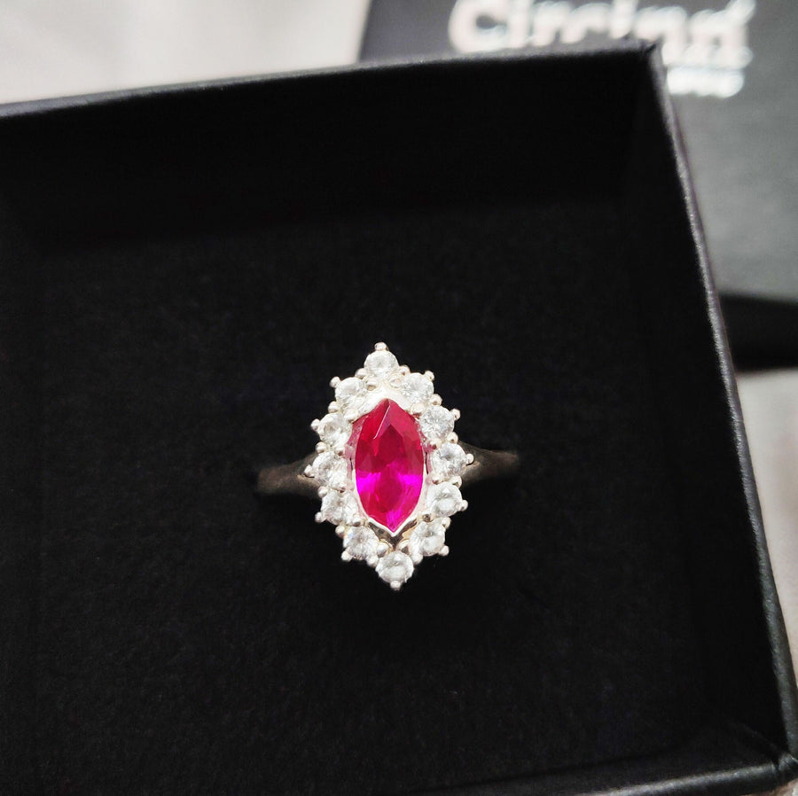 Top view of a marquise ruby and white sapphire pave set cluster halo ring in a branded Circinn ring box.