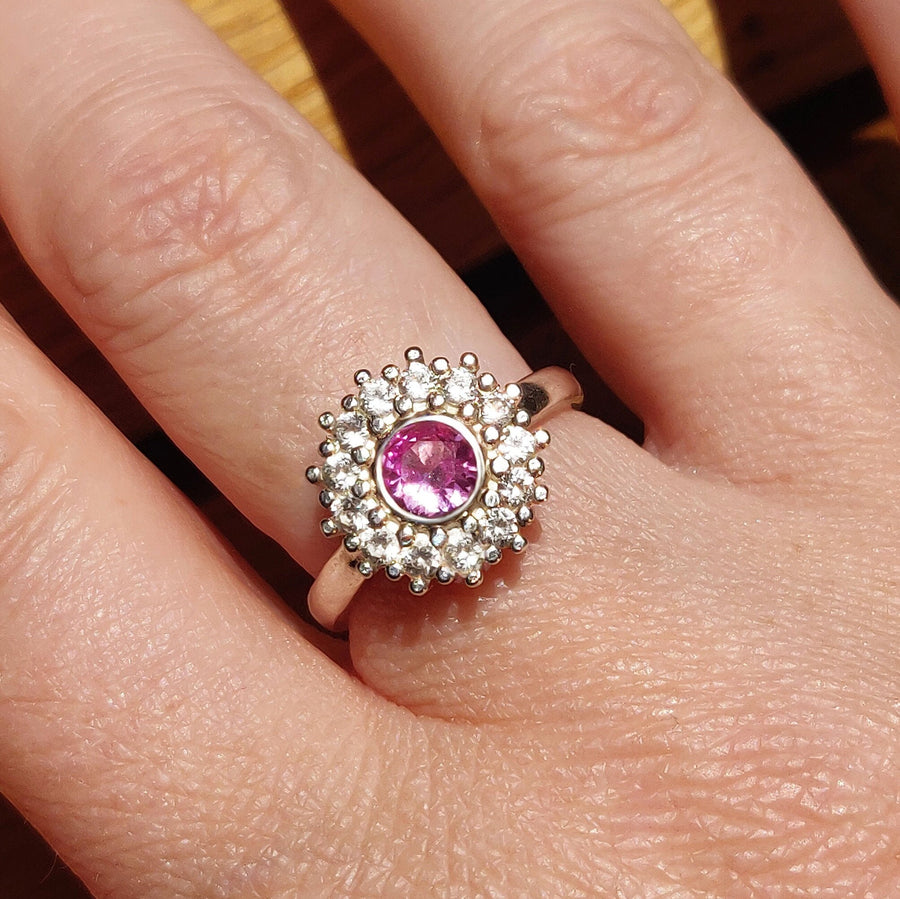 Top view of a pink and white sapphire pave cluster halo ring being worn on a finger.