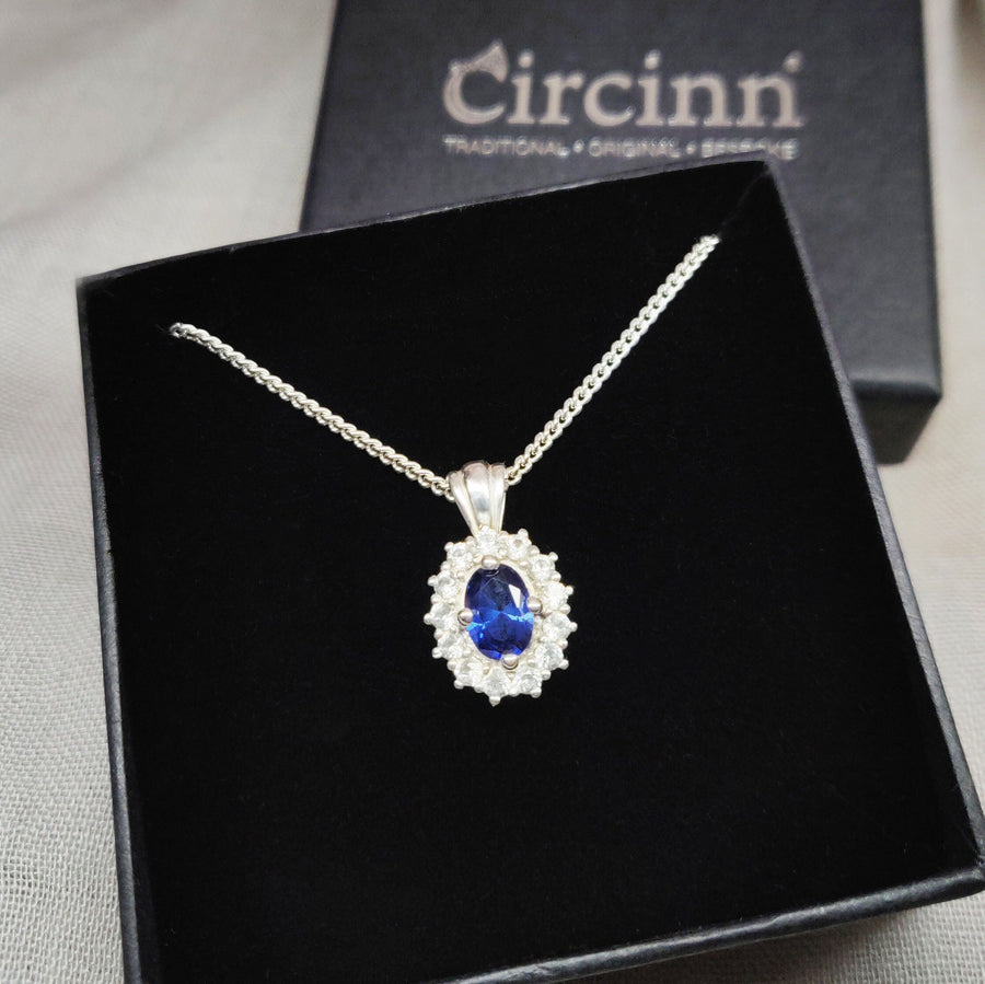 An oval blue sapphire necklace with white sapphire cluster in a display box.