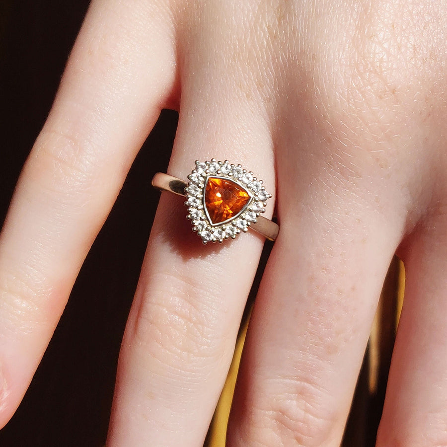 Top view of a trillion cut citrine and white sapphire halo cluster pave ring being worn on a finger.