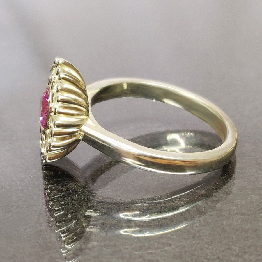 Side view of a pink and white sapphire pave cluster halo ring on a reflective surface.