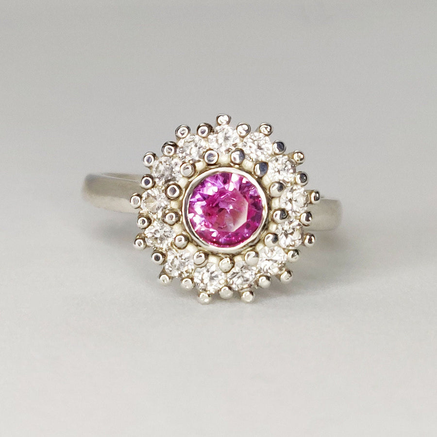 Front view of apink and white sapphire pave cluster halo ring on a white background.