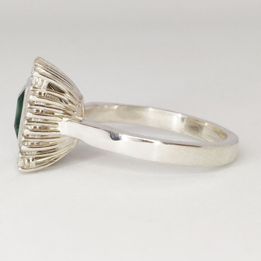Side view of a princess cut emerald and diamond halo cluster ring on a white background.