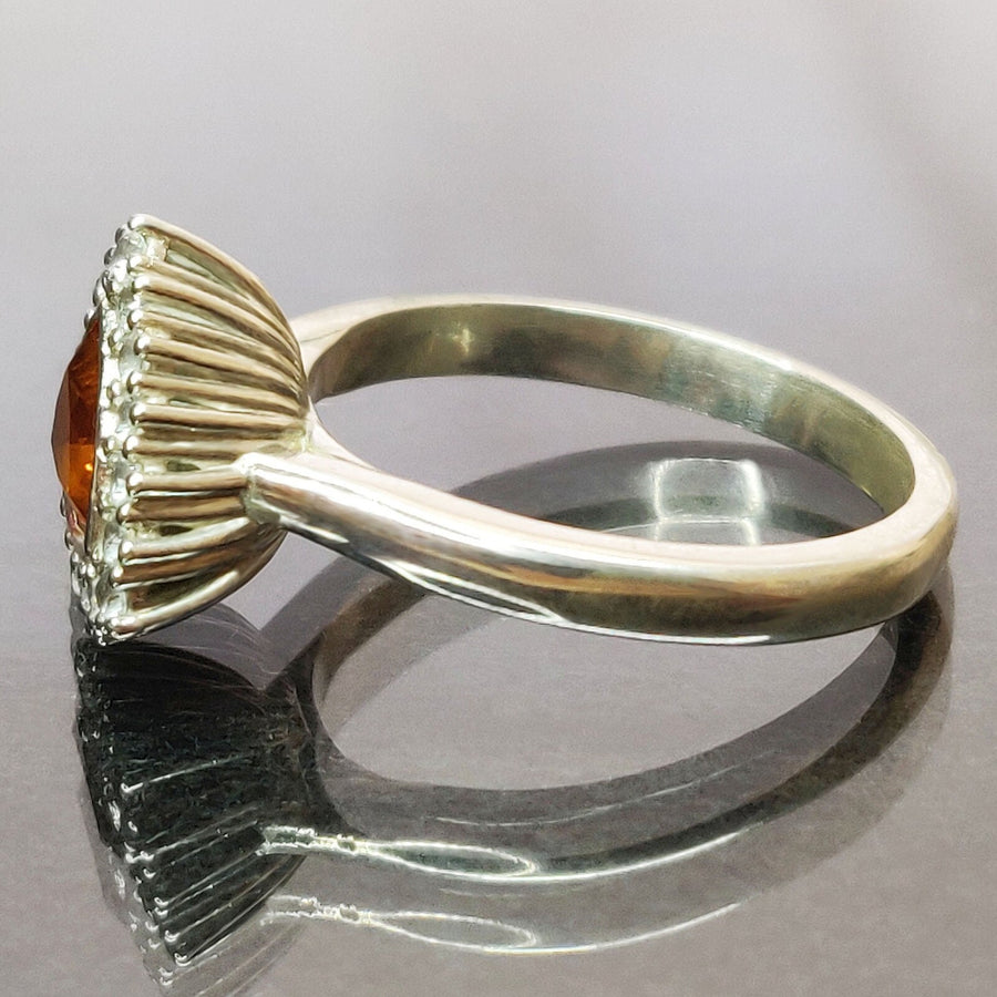 Side view of a trillion cut citrine and white sapphire halo cluster pave ring on a reflective surface.