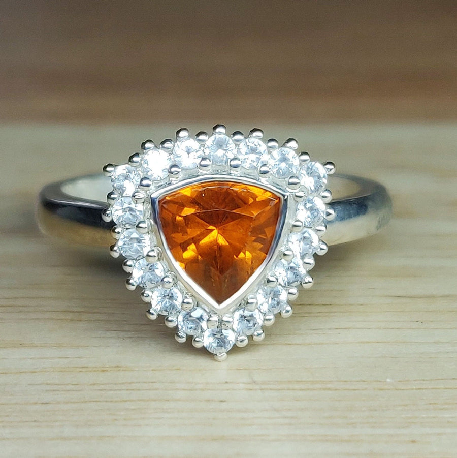 Front view of a trillion cut citrine and white sapphire halo cluster pave ring on a wooden background.