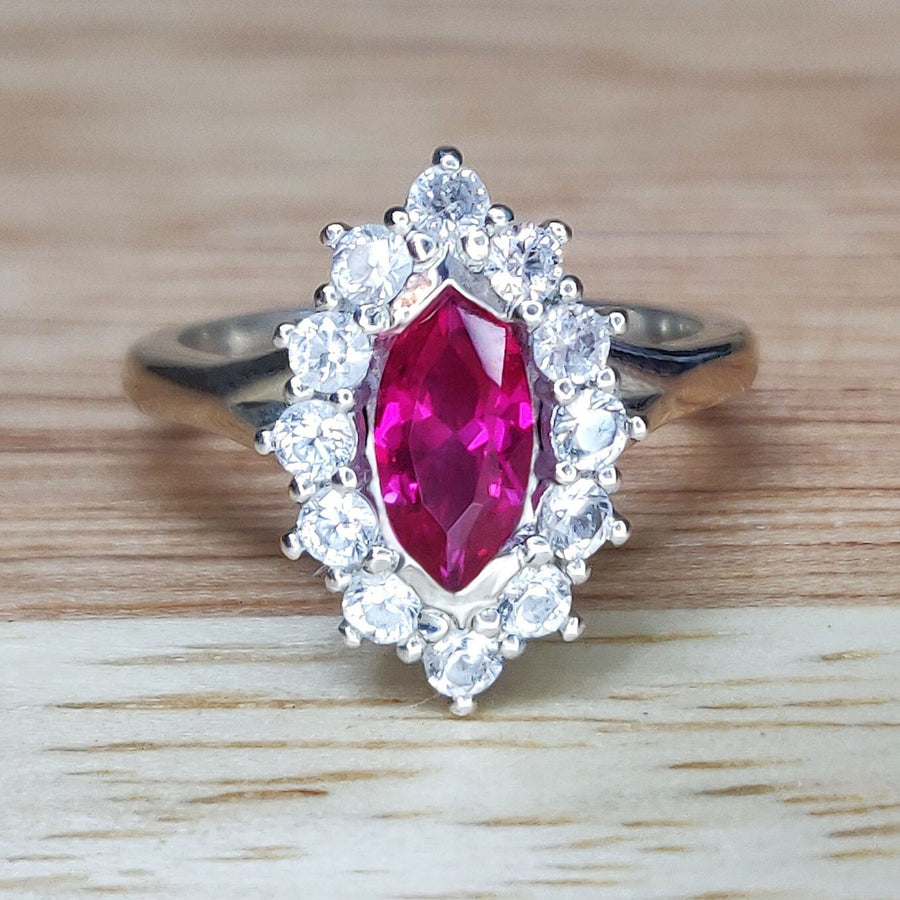 Front view of a marquise ruby and white sapphire pave set cluster halo ring on a wooden background.