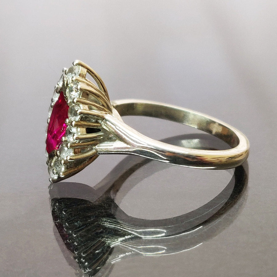 Profile view of a marquise ruby and white sapphire pave set cluster halo ring on a reflective surface.