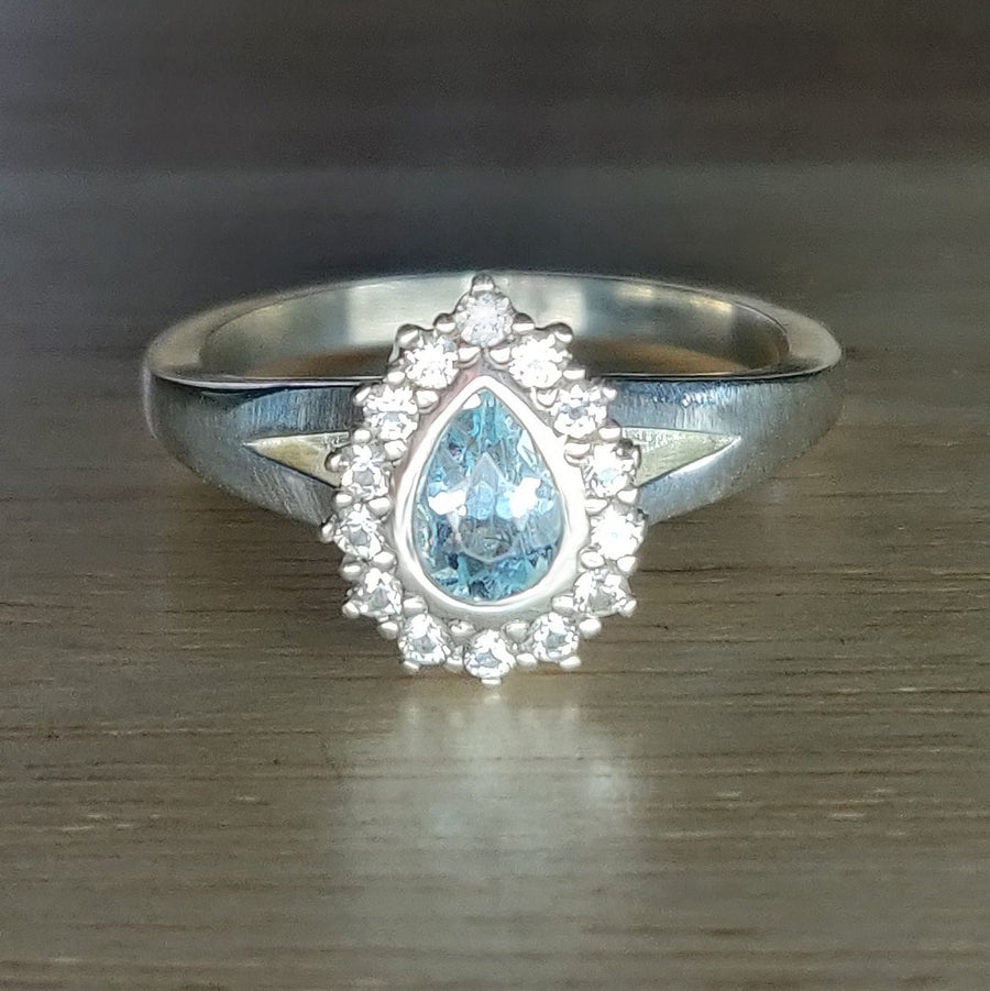 Pear cut aquamarine and white sapphire halo cluster ring on a wooden surface.