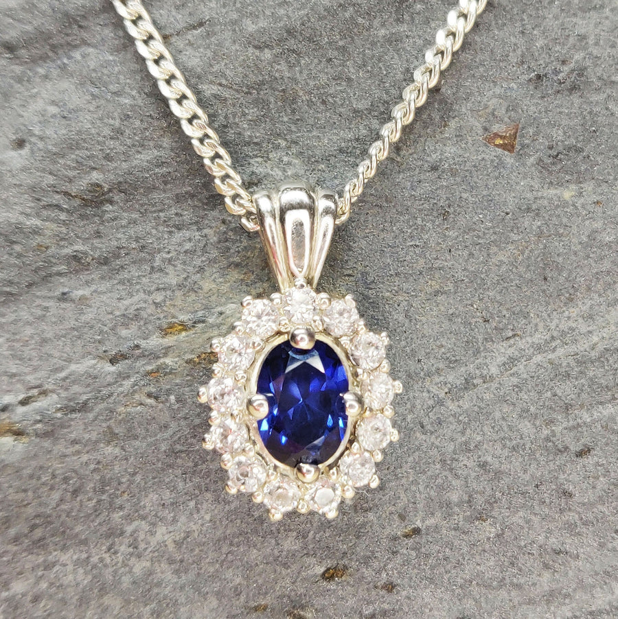Blue and white sapphire pendant in argentium silver on a curb chain, hanging on a slate background.