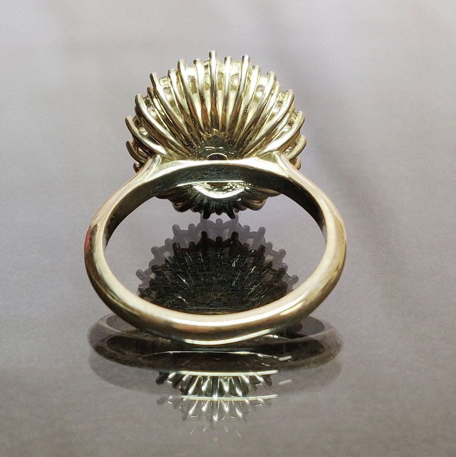 Rear view of a bezel set blue and white sapphire halo cluster ring on a reflective surface.