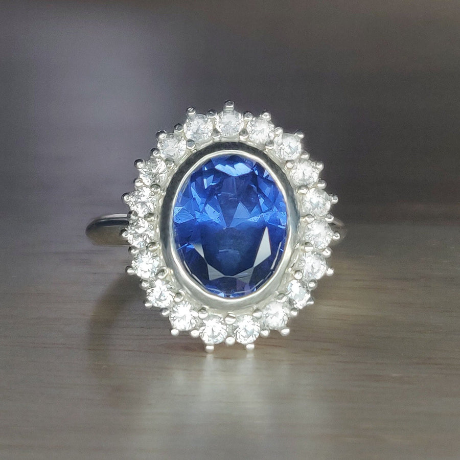 Front view of a Bezel set blue and white sapphire halo cluster ring on a wooden surface.