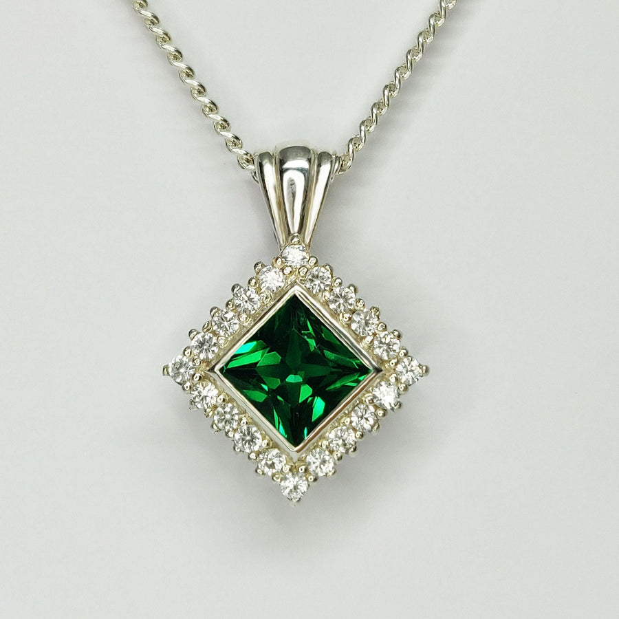 Close up of a Princess Emerald and Diamond Halo Necklace on a white background