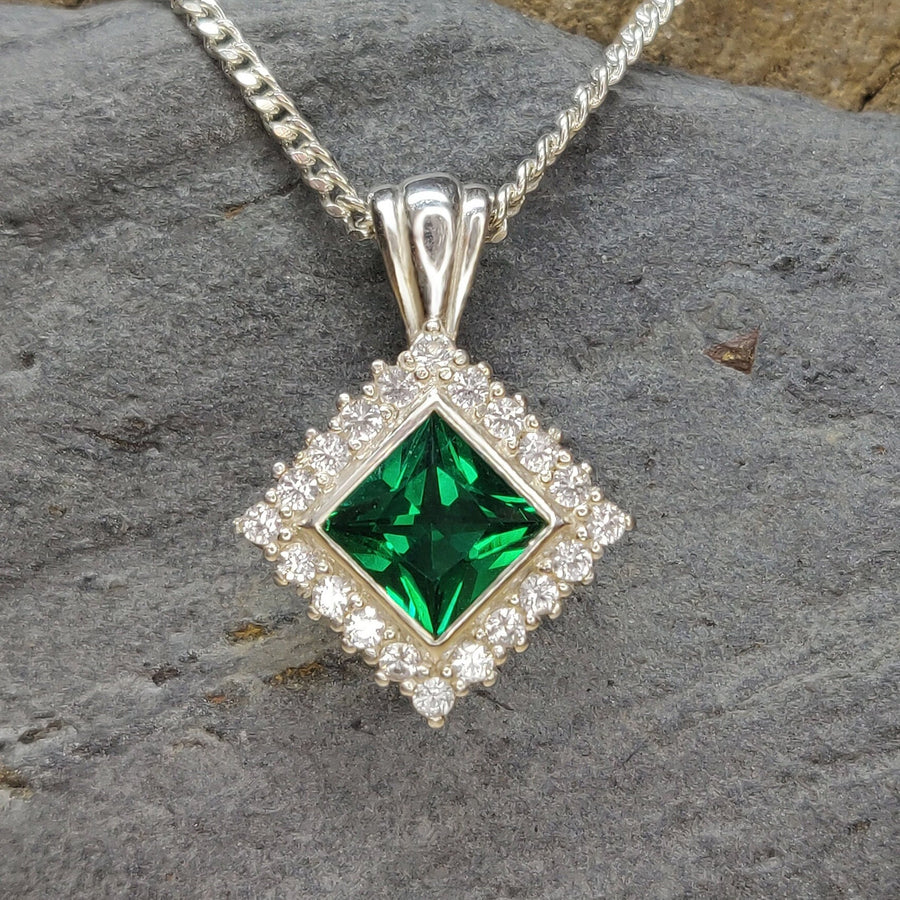 Close up of a Princess Emerald and Diamond Halo Necklace on a slate background