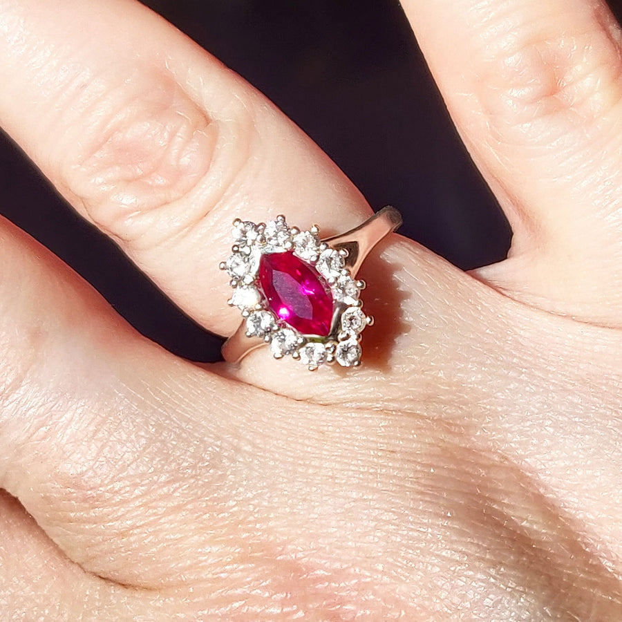 Top view of a marquise ruby and white sapphire pave set cluster halo ring being worn on a finger.