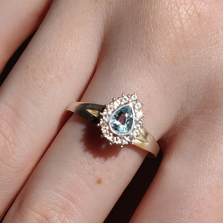 Pear cut aquamarine and white sapphire halo cluster ring being worn on a finger.