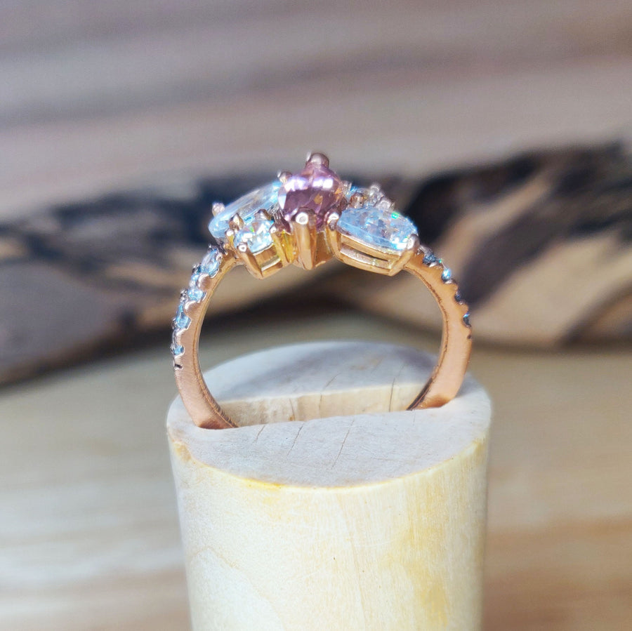 Through finger shot of a Bi Colour Tourmaline and lab-grown diamond gold engagement ring on a wooden stand.