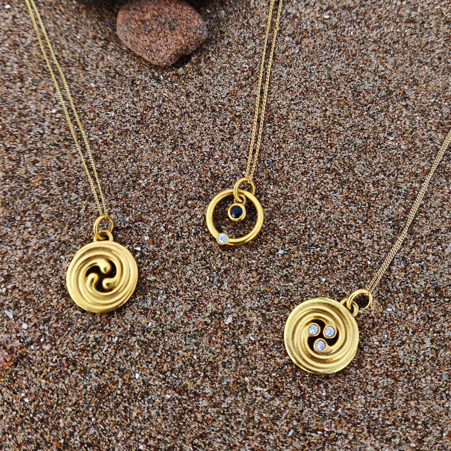 Trio of celtic knot diamond and solid gold necklaces in the sand.