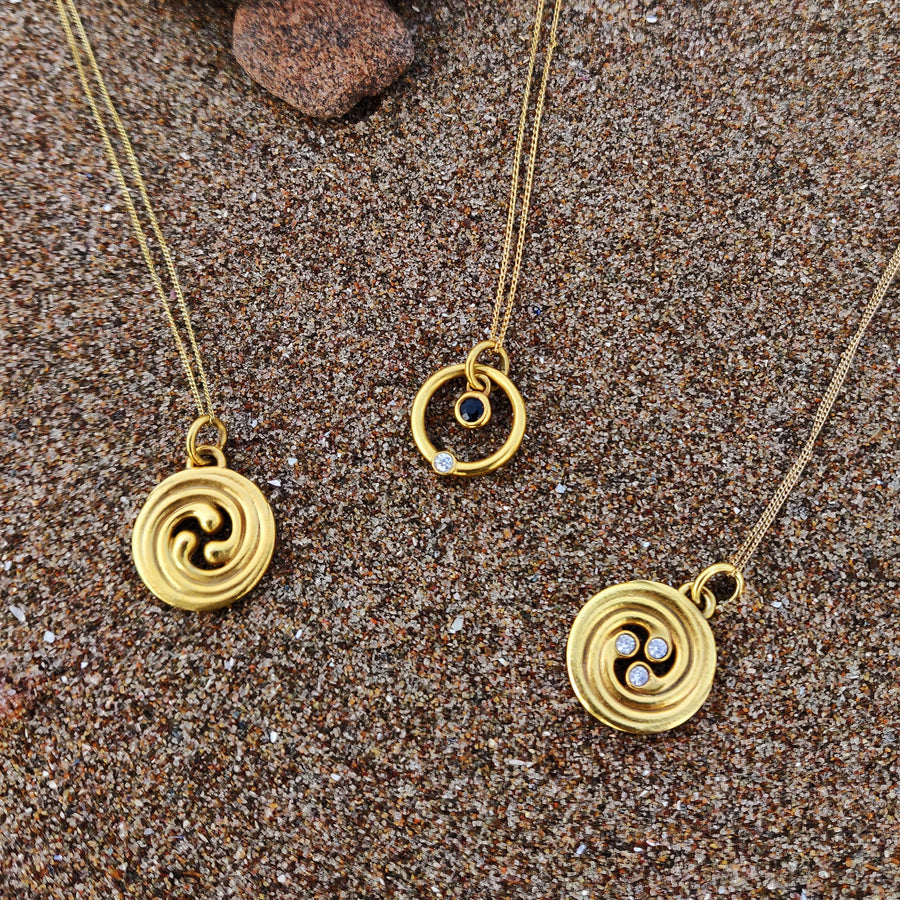3 styles of solid gold celtic necklaces on the sand.