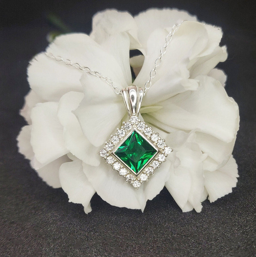 Close up of a Princess Emerald and Diamond Cluster Necklace on a flower