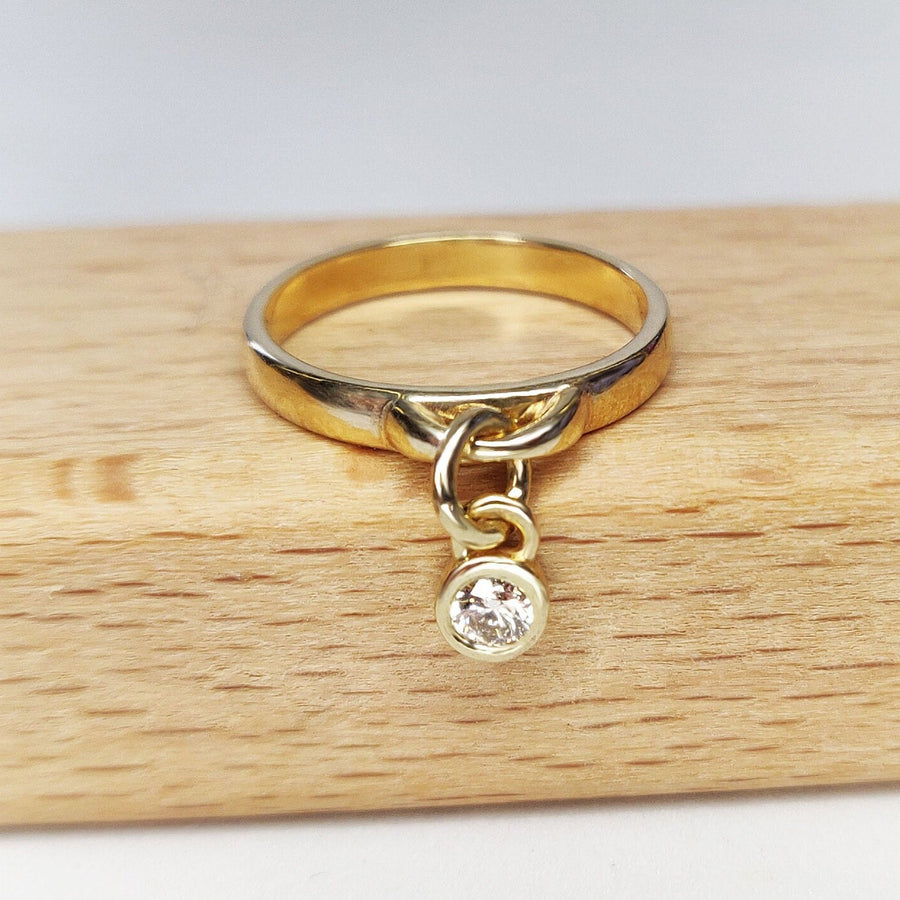 Image of a diamond bezel charm ring in solid yellow gold on a wooden background