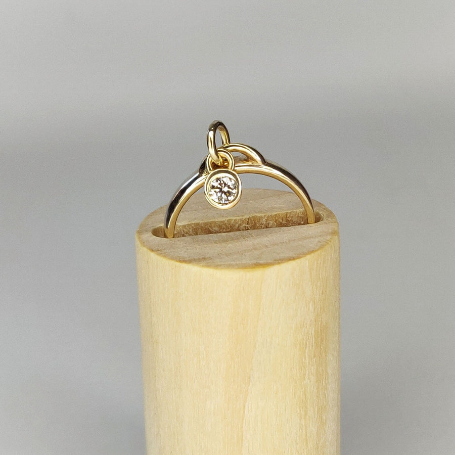 Gold Diamond Dangle Ring With Charm on a wooden display block.