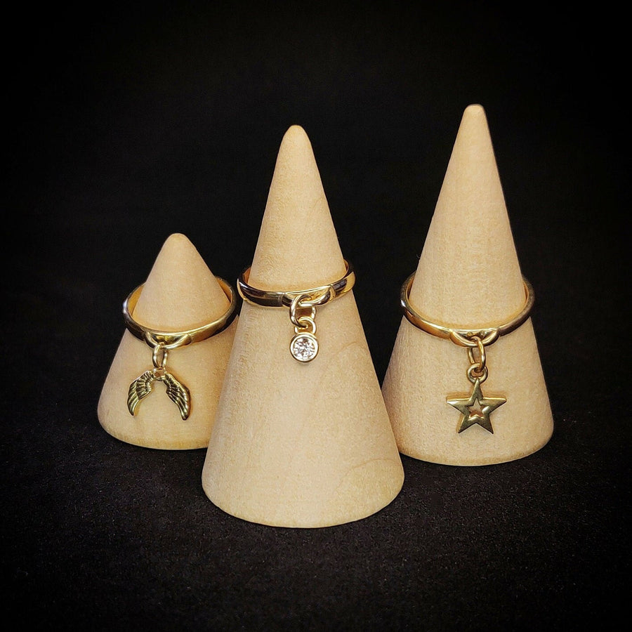 Selection of solid gold rings with diamond, angel wings and star charms - all on wooden display cones against a black background.