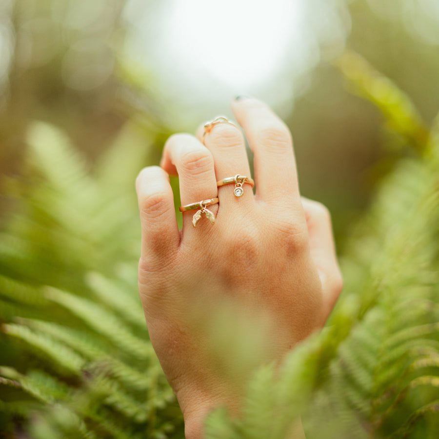 Image of a hand wearing  solid gold dangle rings with diamond and angel wings solid gold charms