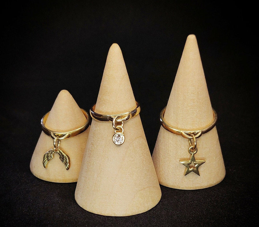 Solid Gold Diamond, Angel Wings and Star Charm Rings on wooden cones against a black background.