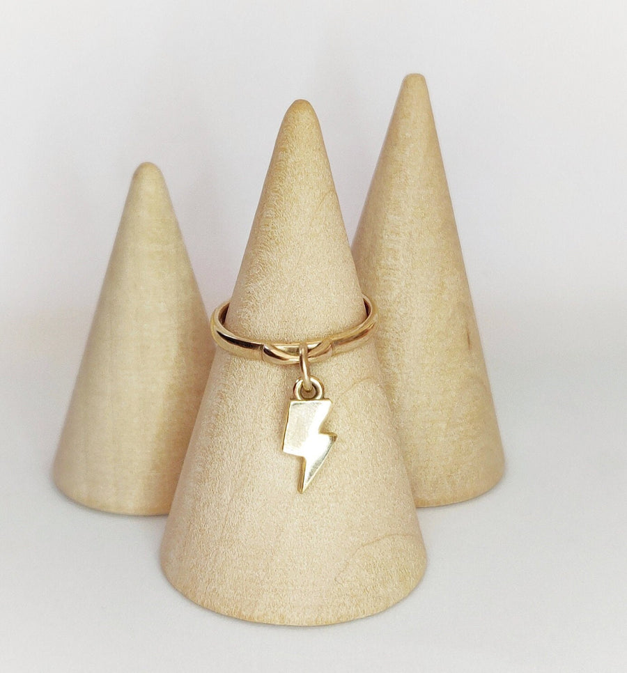 Gold dangle ring with a lightning bolt charm on a wooden display