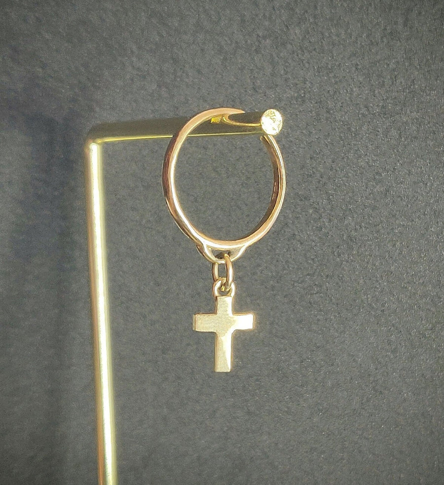 Solid gold dangle ring with cross charm on a display.