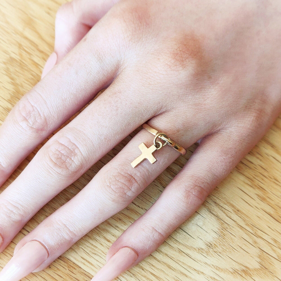 Hand wearing a solid gold cross charm ring.